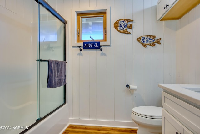 full bathroom featuring wood walls, toilet, shower / bath combination with glass door, vanity, and hardwood / wood-style flooring