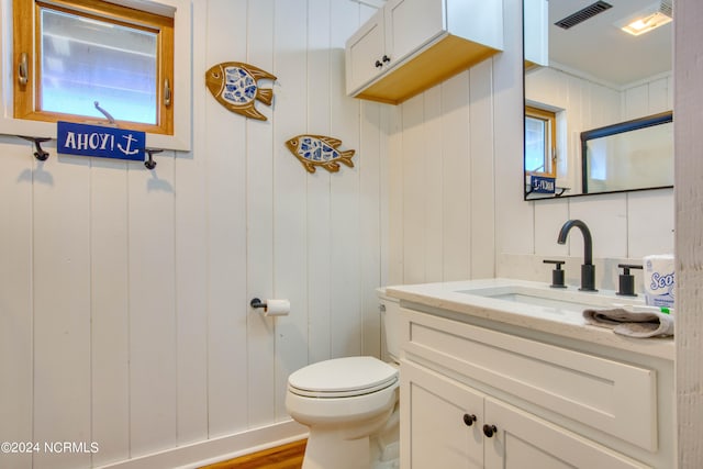 bathroom featuring vanity, toilet, and wooden walls