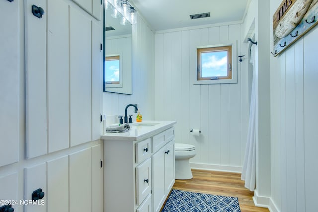 bathroom with hardwood / wood-style floors, vanity, wood walls, and toilet