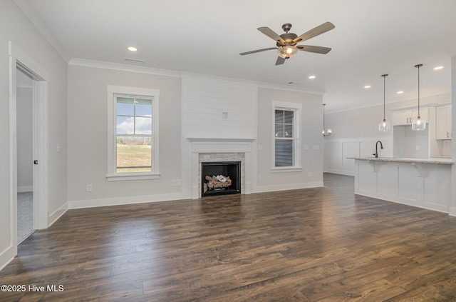 unfurnished living room featuring ceiling fan, sink, dark hardwood / wood-style flooring, a fireplace, and ornamental molding