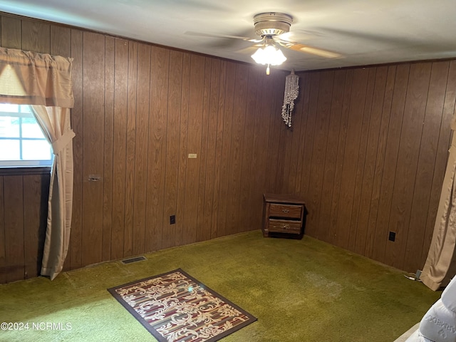 unfurnished room featuring wood walls, carpet flooring, visible vents, and a ceiling fan