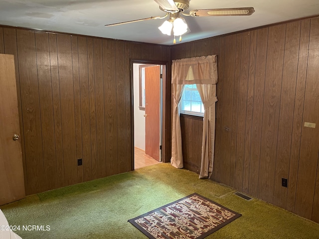 spare room featuring carpet, wooden walls, visible vents, and ceiling fan