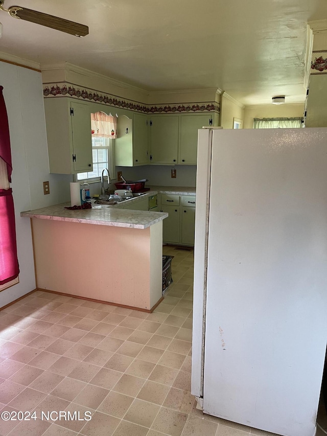 kitchen featuring a peninsula, a sink, light countertops, freestanding refrigerator, and green cabinetry