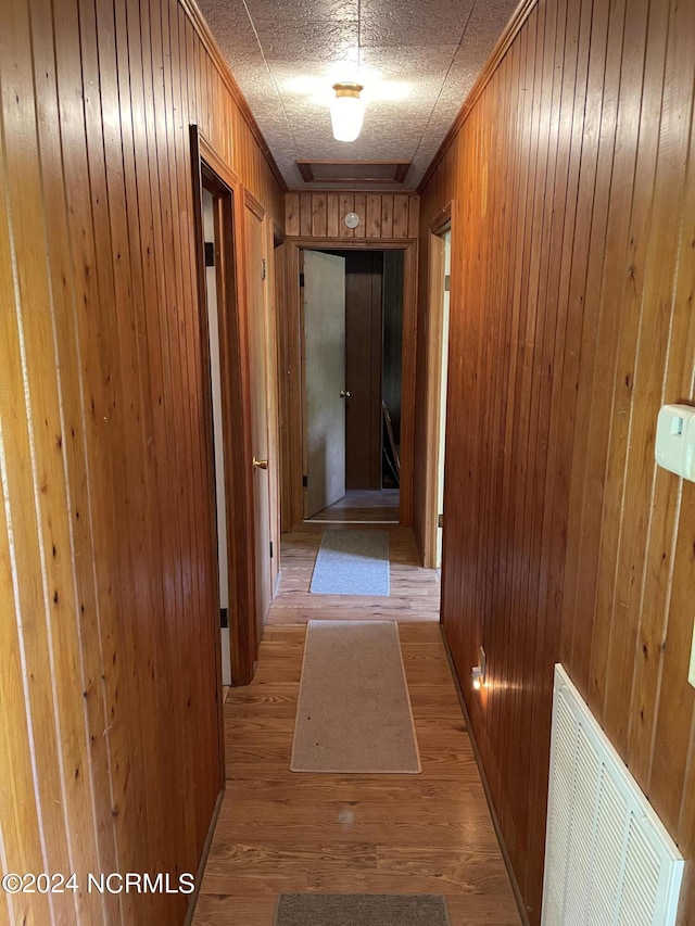 corridor featuring ornamental molding, wood walls, light wood-type flooring, and visible vents