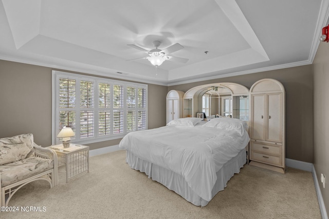 bedroom featuring ceiling fan, ornamental molding, light carpet, and a tray ceiling