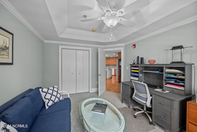 carpeted home office featuring ornamental molding, a tray ceiling, and ceiling fan