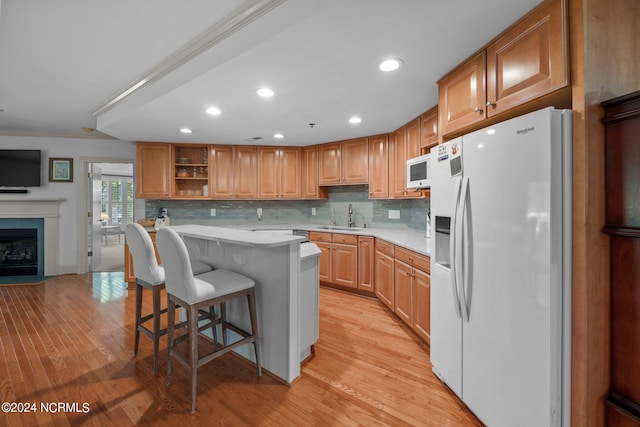 kitchen with a kitchen breakfast bar, white appliances, light hardwood / wood-style flooring, crown molding, and sink