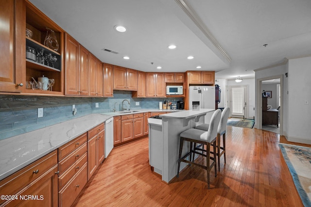 kitchen featuring white appliances, light hardwood / wood-style flooring, a kitchen bar, a center island, and sink