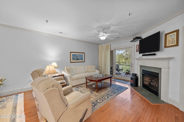 living room featuring ornamental molding, ceiling fan, a tiled fireplace, and light wood-type flooring