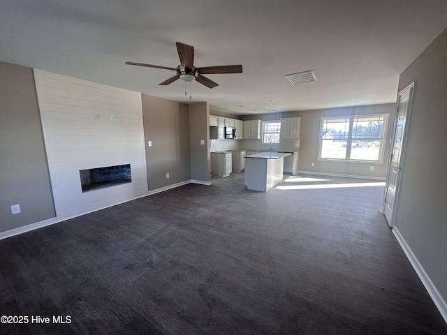 unfurnished living room with ceiling fan, a large fireplace, and dark hardwood / wood-style floors