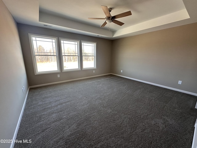 spare room featuring ceiling fan, a tray ceiling, and dark colored carpet