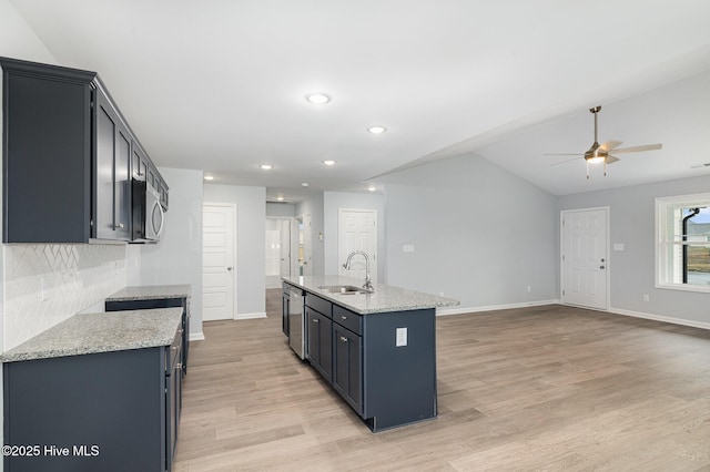 kitchen featuring sink, light hardwood / wood-style flooring, stainless steel appliances, light stone countertops, and a center island with sink