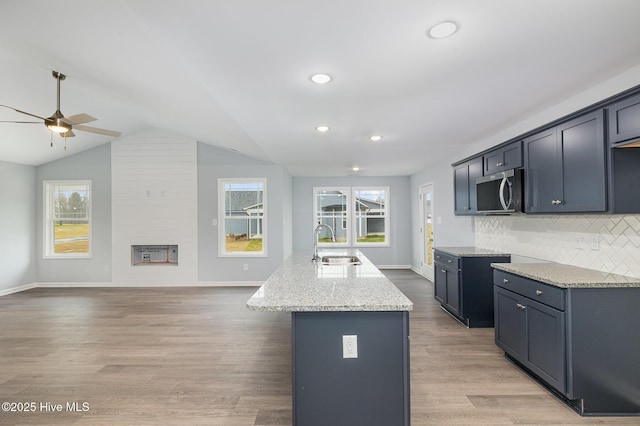 kitchen featuring sink, hardwood / wood-style flooring, backsplash, light stone countertops, and an island with sink