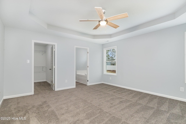 unfurnished bedroom featuring ensuite bath, carpet floors, a raised ceiling, a walk in closet, and a closet