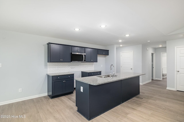 kitchen with sink, light stone counters, tasteful backsplash, light hardwood / wood-style floors, and a center island with sink