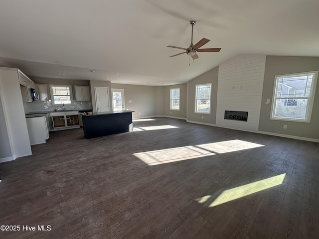 unfurnished living room featuring ceiling fan, vaulted ceiling, dark hardwood / wood-style floors, a large fireplace, and sink