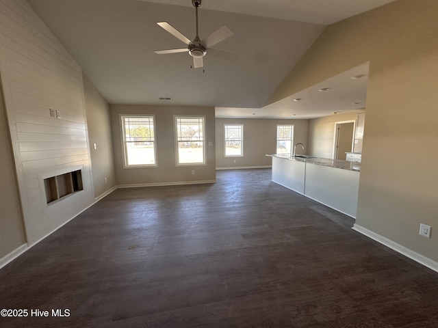 unfurnished living room featuring lofted ceiling, dark wood-type flooring, a fireplace, sink, and ceiling fan