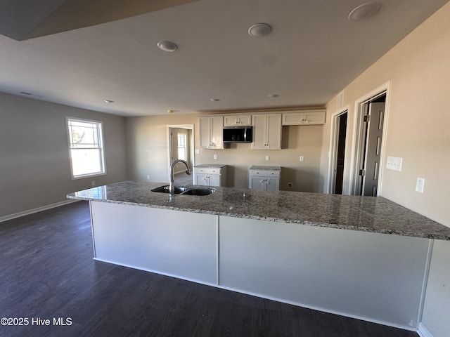 kitchen with white cabinets, dark wood-type flooring, sink, and light stone counters