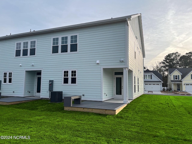 rear view of property featuring a garage, a patio, a yard, and central AC