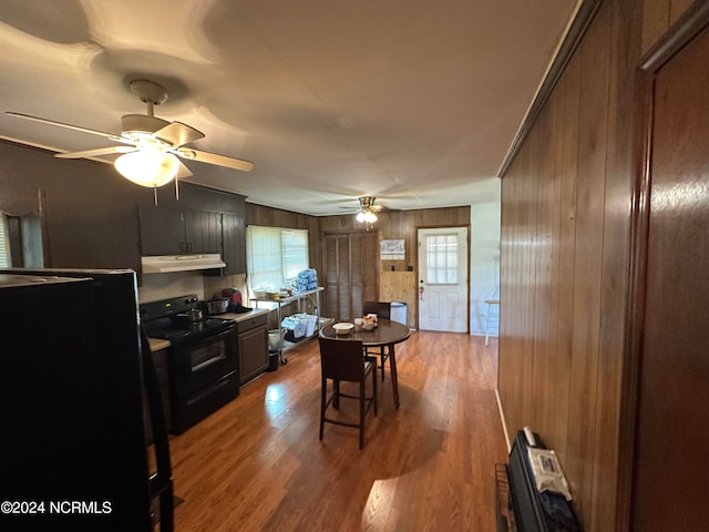 kitchen featuring ceiling fan, wooden walls, hardwood / wood-style flooring, and black electric range