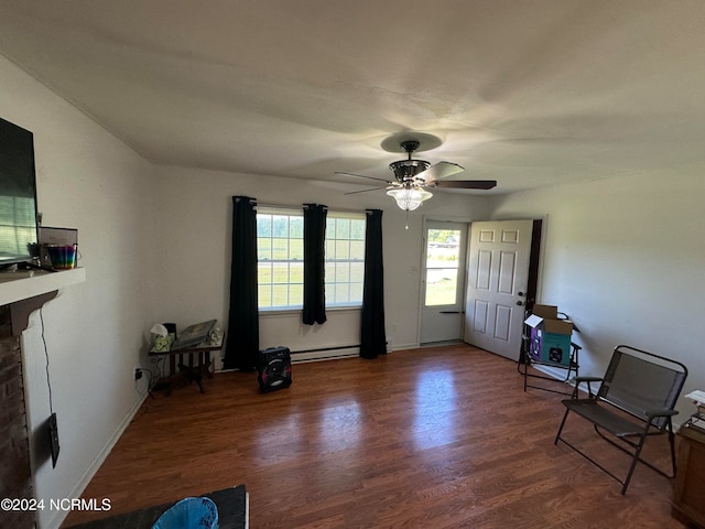 sitting room featuring ceiling fan, dark hardwood / wood-style flooring, baseboard heating, and a brick fireplace