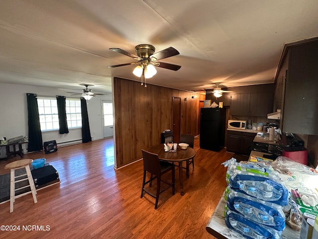 living room with wooden walls, ceiling fan, a baseboard radiator, and wood-type flooring