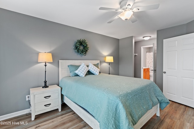 bedroom featuring wood finished floors, ensuite bath, baseboards, and a ceiling fan