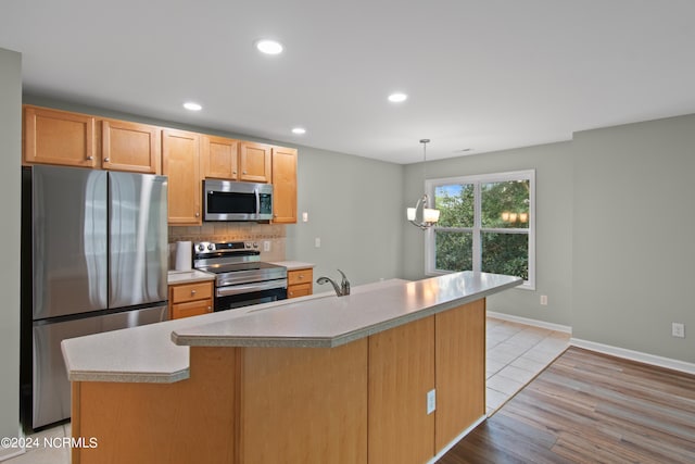 kitchen with a center island with sink, hanging light fixtures, light wood-type flooring, tasteful backsplash, and stainless steel appliances