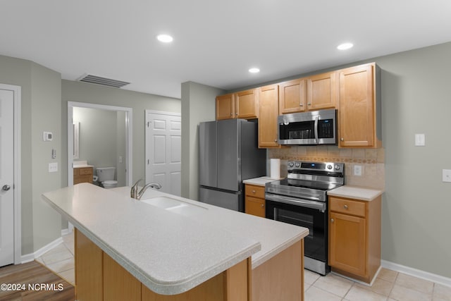 kitchen with backsplash, a center island with sink, sink, light tile patterned flooring, and stainless steel appliances