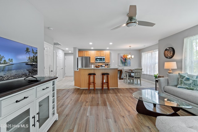 living area featuring light wood finished floors, a chandelier, recessed lighting, a ceiling fan, and baseboards