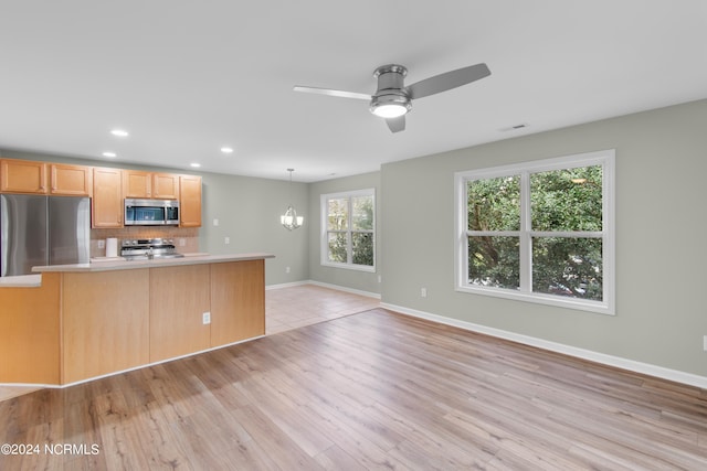 kitchen with hanging light fixtures, tasteful backsplash, light hardwood / wood-style floors, ceiling fan with notable chandelier, and appliances with stainless steel finishes