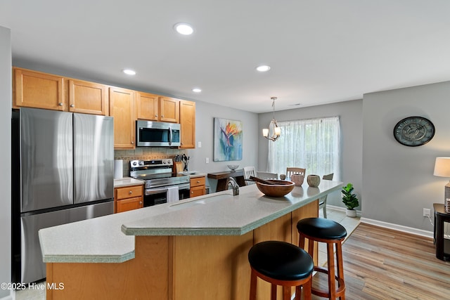 kitchen featuring appliances with stainless steel finishes, a sink, baseboards, backsplash, and a breakfast bar