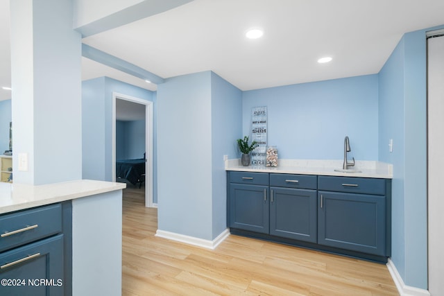 bar featuring blue cabinetry, light hardwood / wood-style flooring, and sink