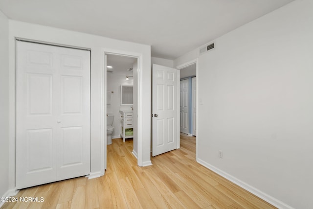 unfurnished bedroom with ensuite bathroom, light hardwood / wood-style flooring, and a closet