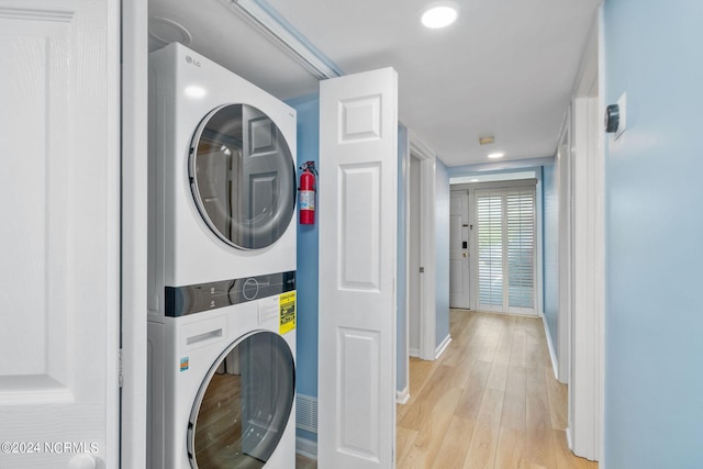 washroom with stacked washing maching and dryer and light wood-type flooring