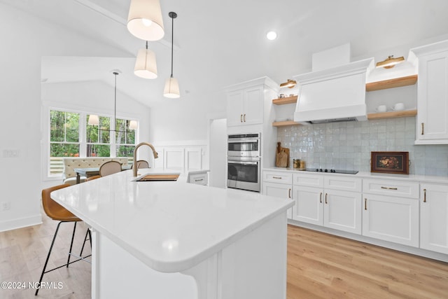 kitchen with white cabinets, a center island with sink, a kitchen breakfast bar, pendant lighting, and sink