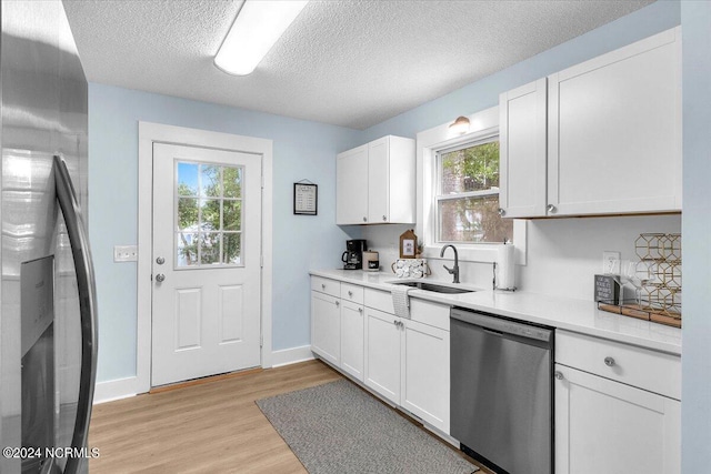 kitchen featuring appliances with stainless steel finishes, a textured ceiling, sink, light hardwood / wood-style floors, and white cabinetry