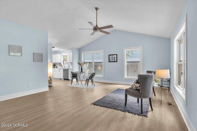 living area featuring a textured ceiling, light wood-type flooring, vaulted ceiling, and ceiling fan