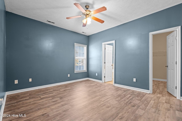 unfurnished bedroom with ceiling fan, light hardwood / wood-style floors, a walk in closet, and a textured ceiling