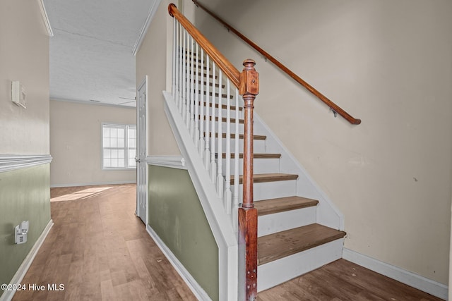 stairs featuring wood-type flooring, a textured ceiling, and ornamental molding