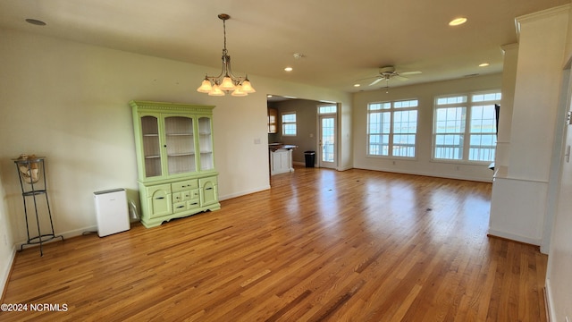 unfurnished living room featuring ceiling fan with notable chandelier and light hardwood / wood-style floors