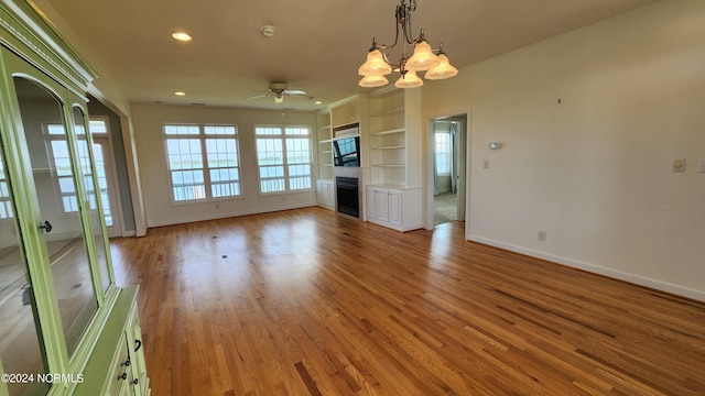 unfurnished living room featuring built in features, ceiling fan with notable chandelier, and light hardwood / wood-style flooring