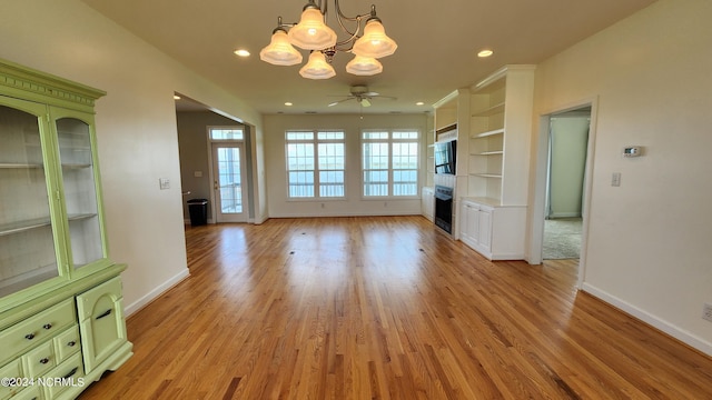 unfurnished living room with built in shelves, ceiling fan with notable chandelier, and light hardwood / wood-style floors