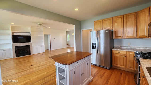 kitchen with light stone countertops, ceiling fan, stainless steel appliances, light hardwood / wood-style flooring, and a tiled fireplace