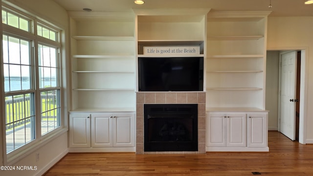 unfurnished living room with built in shelves, a water view, light hardwood / wood-style flooring, and a tiled fireplace