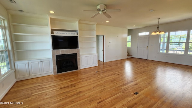 unfurnished living room with built in features, ceiling fan with notable chandelier, light hardwood / wood-style flooring, and a tiled fireplace