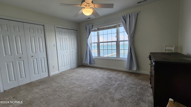 carpeted bedroom featuring two closets, a water view, and ceiling fan