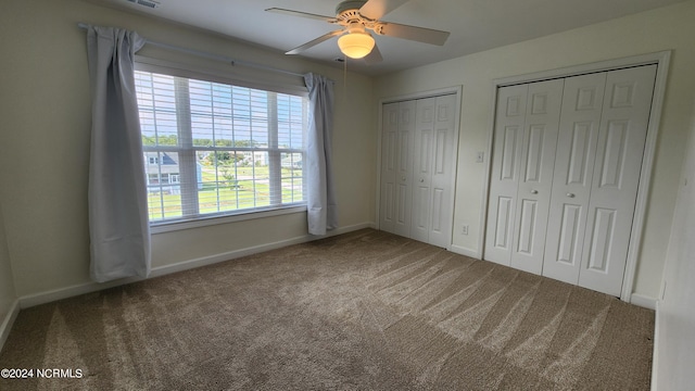 unfurnished bedroom featuring carpet, two closets, multiple windows, and ceiling fan