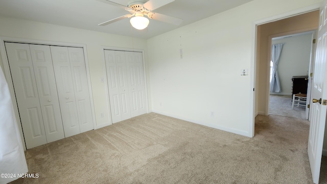 unfurnished bedroom with light colored carpet, ceiling fan, and multiple closets