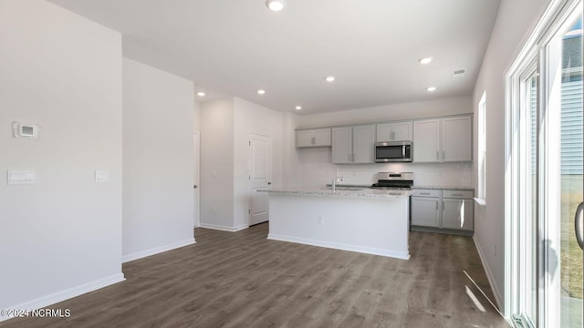 kitchen featuring light stone countertops, an island with sink, gray cabinets, appliances with stainless steel finishes, and hardwood / wood-style flooring